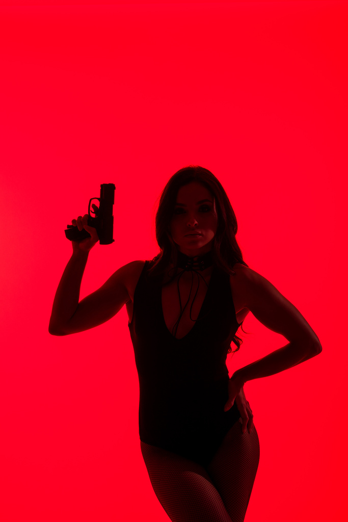 силует красивої жінки в боді-костюмі тримає пістолет ізольовано на червоному
 - Фото, зображення