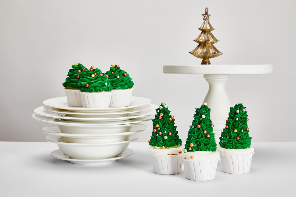 leckere Weihnachtsbaum-Cupcakes mit Tellern auf weißer Oberfläche isoliert auf grau - Foto, Bild