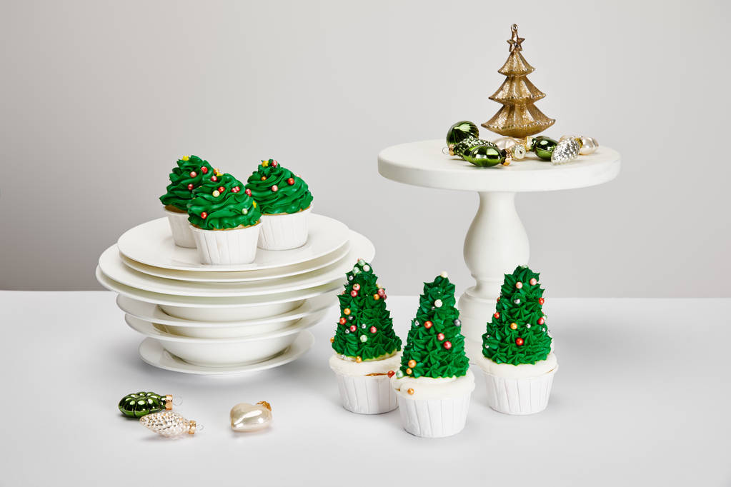 délicieux cupcakes de sapin de Noël avec assiettes et boules brillantes sur surface blanche isolée sur gris
 - Photo, image