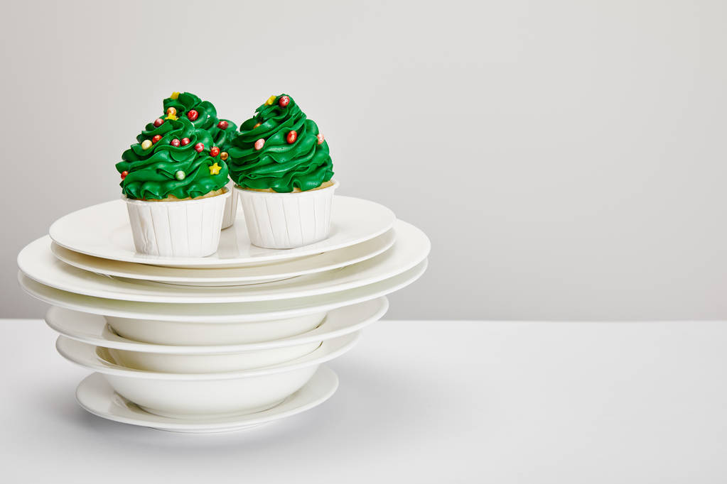 leckere Weihnachtsbaum-Cupcakes mit Tellern auf weißer Oberfläche isoliert auf grau - Foto, Bild