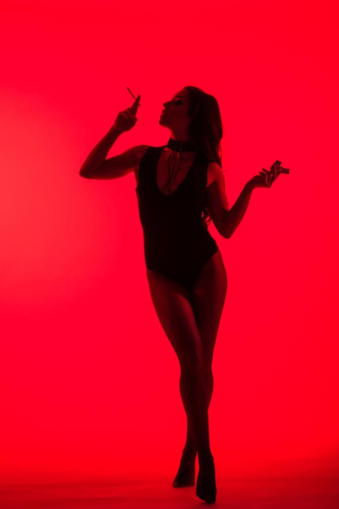 силует сексуальної дівчини тримає легшу куріння сигарету ізольовано на червоному
  - Фото, зображення