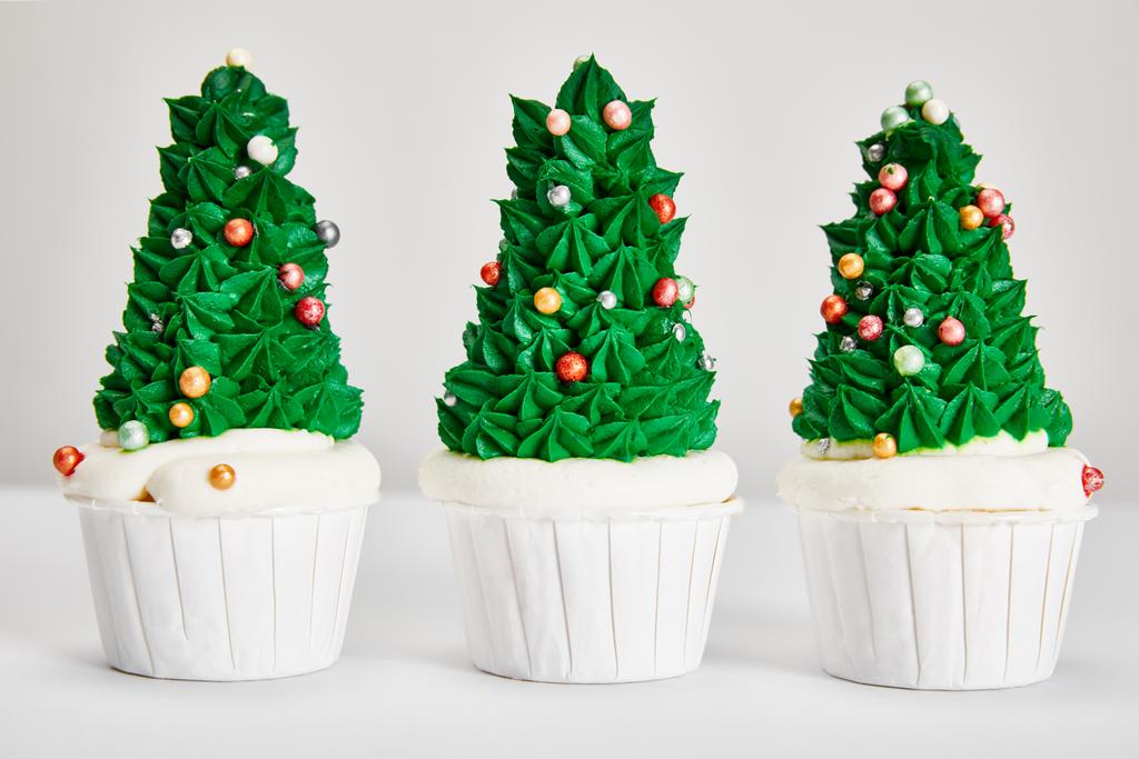 leckere Weihnachtsbaum-Cupcakes in Reihe auf weißer Oberfläche isoliert auf grau - Foto, Bild