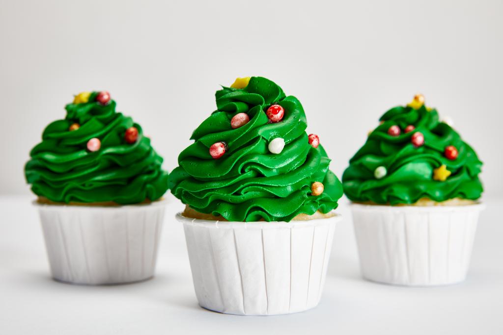 selective focus of tasty Christmas tree cupcakes in row on white surface isolated on grey - Photo, Image