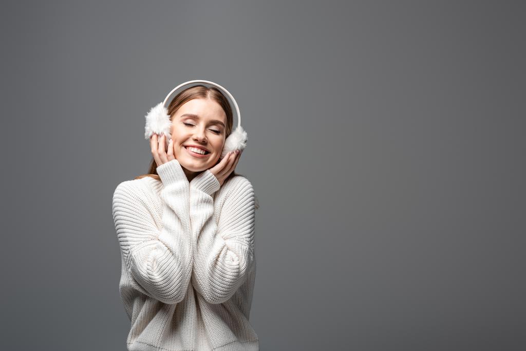 ελκυστικό χαμογελαστό κορίτσι ποζάρουν σε λευκό πουλόβερ και ωτοασπίδες, απομονώνονται σε γκρι - Φωτογραφία, εικόνα