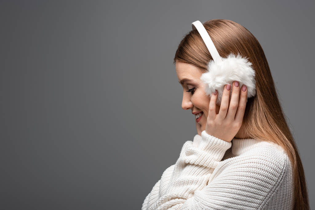 profil portré mosolygós lány pózol fehér pulóver és fülvédő, elszigetelt szürke - Fotó, kép