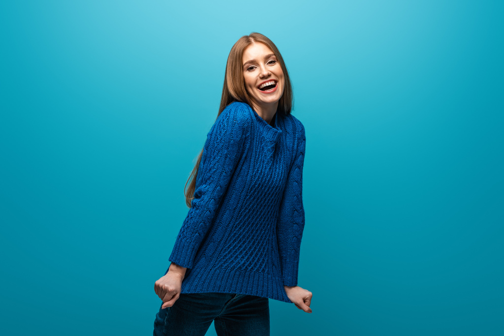 atraktivní pozitivní žena v modrém pleteném svetru, izolovaná na modré - Fotografie, Obrázek