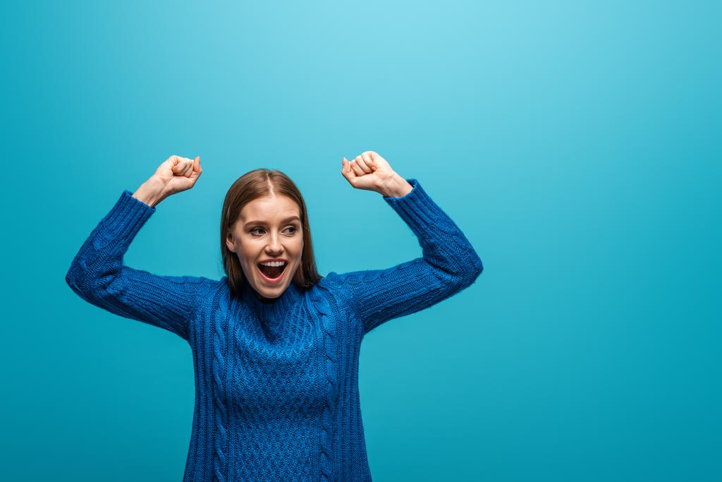 青いニットのセーターを着た魅力的な幸せな女性が成功を祝い - 写真・画像