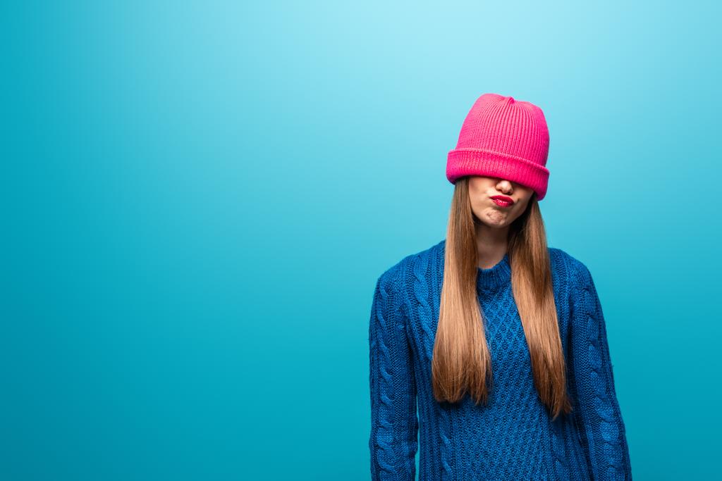jolie femme offensée en pull tricoté avec chapeau rose sur les yeux, isolé sur bleu
 - Photo, image
