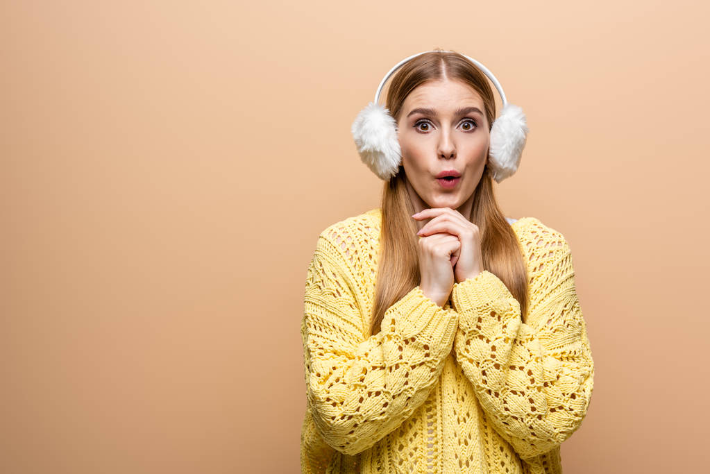 beautiful surprised woman in yellow sweater and ear warmers, isolated on beige - Photo, Image