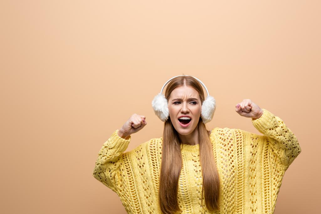 beautiful cheerful woman dancing in yellow sweater and earmuffs, isolated on beige - Photo, Image