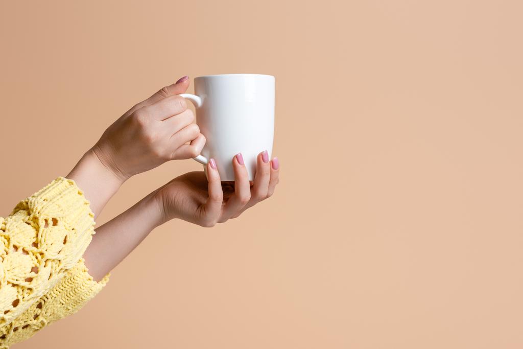 Sarı kazaklı bir kadının elinde kahve fincanı, bej rengi üzerinde izole edilmiş. - Fotoğraf, Görsel