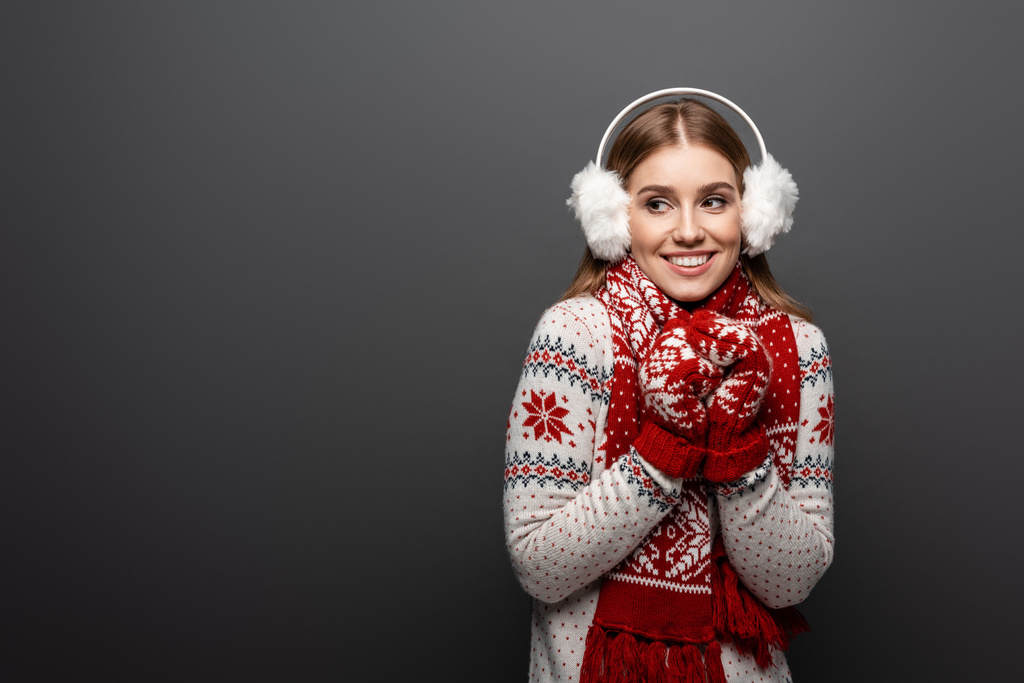 улыбающаяся девушка в рождественском свитере, шарфе, рукавицах и наушниках, изолированная на сером
 - Фото, изображение