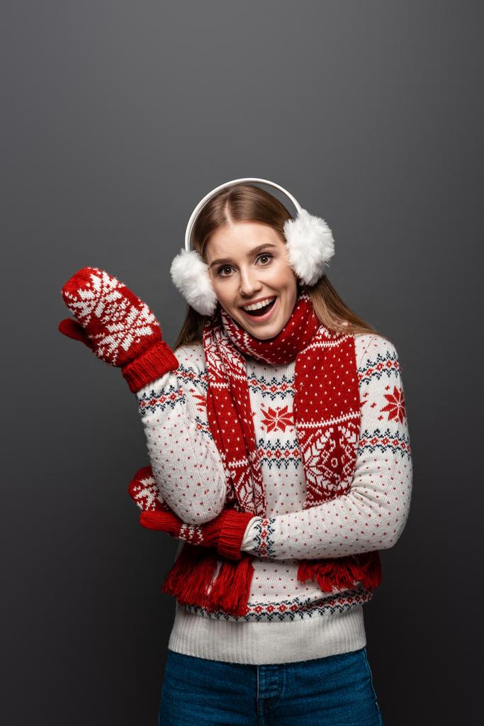 ελκυστική χαρούμενη γυναίκα σε χριστουγεννιάτικο πουλόβερ, μαντήλι, γάντια και ωτοασπίδες, απομονωμένη σε γκρι - Φωτογραφία, εικόνα