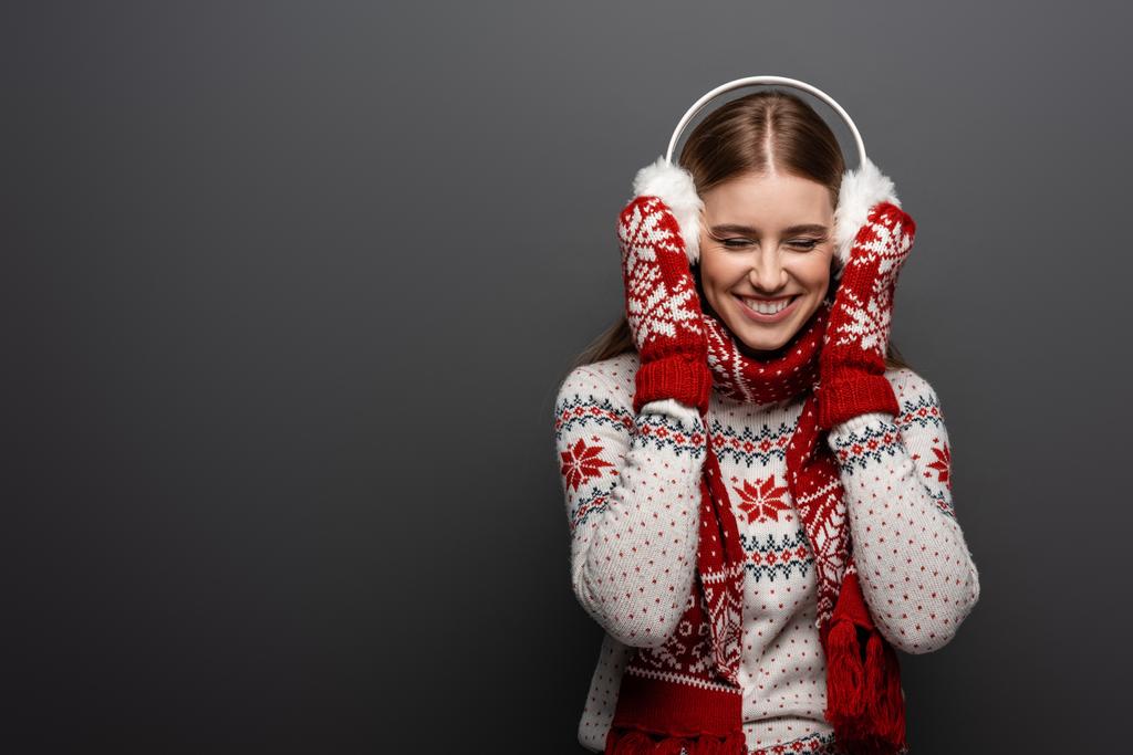 ελκυστική γυναίκα γέλιο σε χριστουγεννιάτικο πουλόβερ, κασκόλ, γάντια και ωτοασπίδες, απομονώνονται σε γκρι - Φωτογραφία, εικόνα