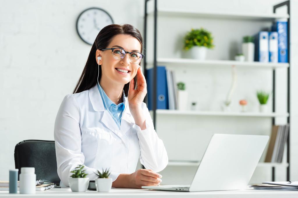 fröhlicher Arzt mit Kopfhörer mit Online-Konsultation mit Patient am Laptop in der Klinik-Praxis - Foto, Bild