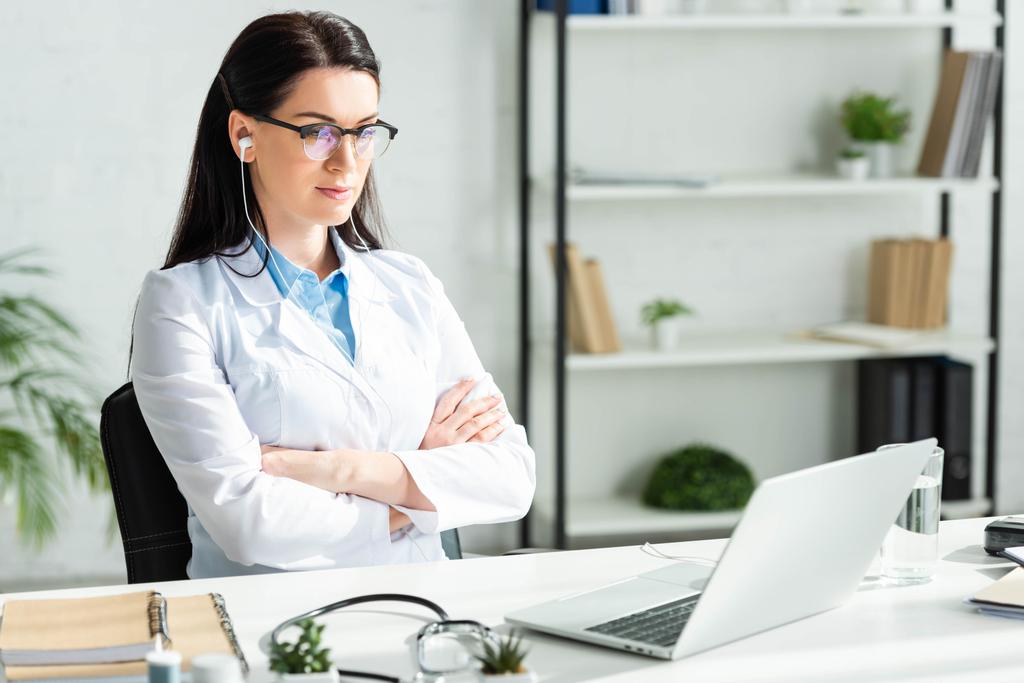 kobieta lekarz z skrzyżowanymi ramionami po konsultacji online z pacjentem na laptopie w gabinecie kliniki - Zdjęcie, obraz