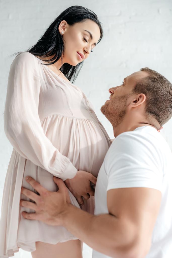 ハンサムな夫が妊娠中の妻をベッドルームで抱きかかえて  - 写真・画像