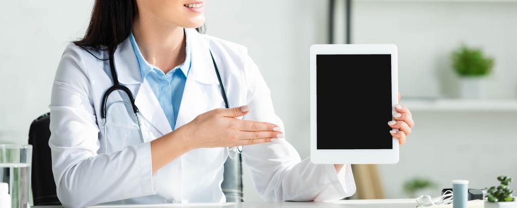 panoráma lövés mosolygós orvos mutatja digitális tabletta üres képernyővel klinika iroda - Fotó, kép