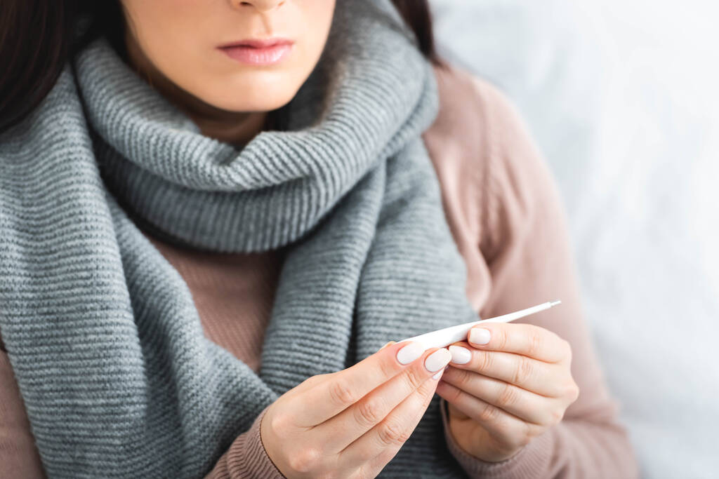bijgesneden zicht op zieke vrouw met thermometer met koorts thuis - Foto, afbeelding