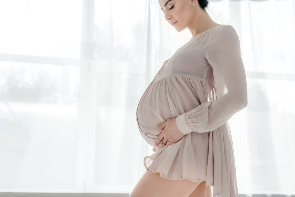 atraktivní šťastná těhotná žena v noční košile dotýkání břicha v ložnici - Fotografie, Obrázek