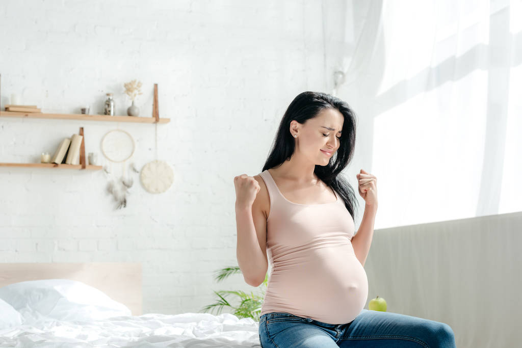 femme enceinte émotionnelle tenant les poings tout en étant assis dans la chambre
 - Photo, image