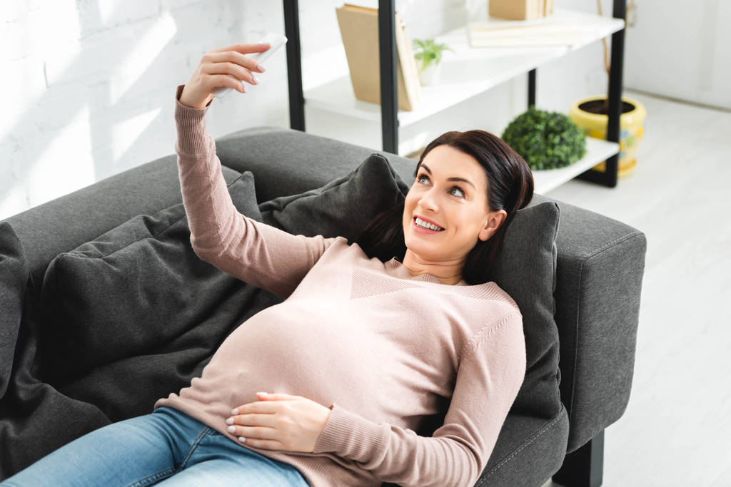 жизнерадостная беременная женщина, имеющая онлайн консультацию с врачом на смартфоне
 - Фото, изображение