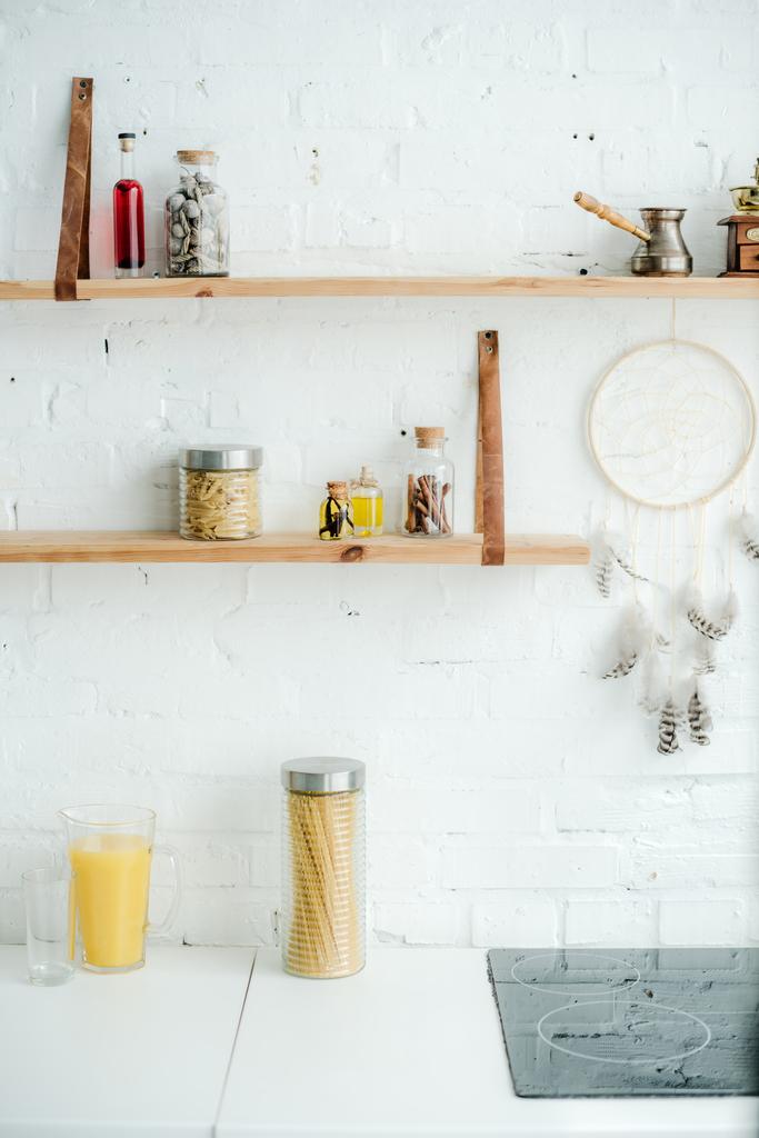 fogão elétrico, apanhador de sonhos e prateleiras de madeira com frascos na parede de tijolo branco na cozinha
 - Foto, Imagem