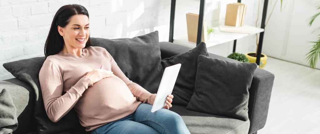 панорамний знімок усміхненої вагітної жінки, що має онлайн-консультацію з лікарем на цифровому планшеті вдома
 - Фото, зображення