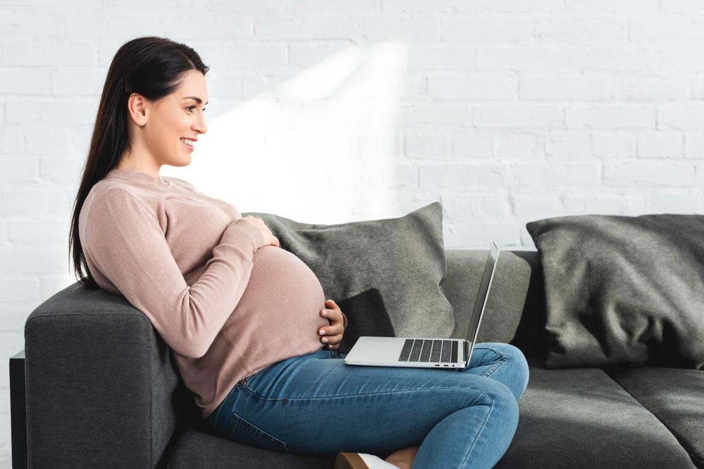 mujer embarazada feliz que tiene consulta en línea con el médico en el ordenador portátil en casa
 - Foto, imagen