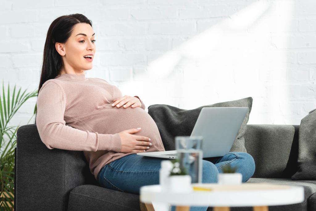 atractiva mujer embarazada que tiene consulta en línea con el médico en el ordenador portátil en casa
 - Foto, imagen