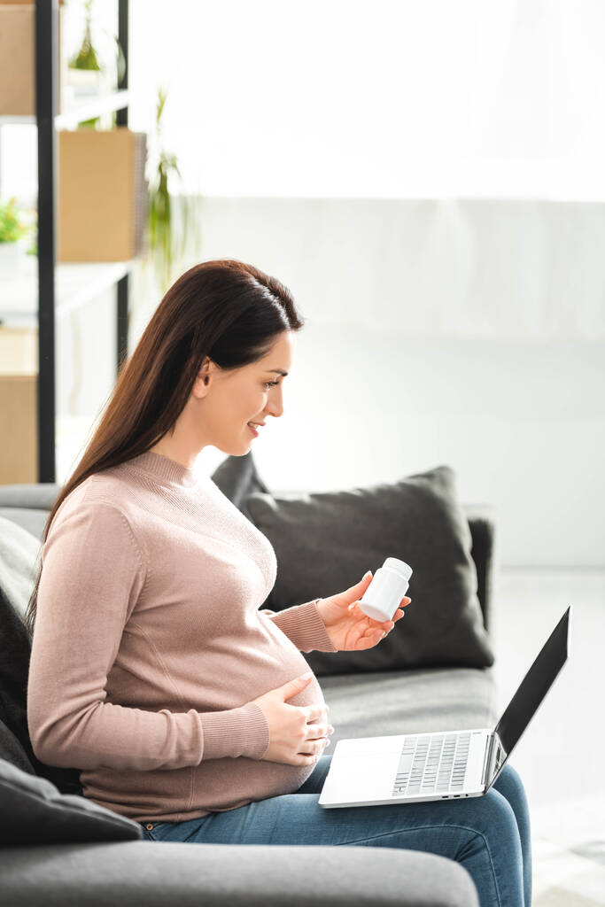 έγκυος γυναίκα κρατώντας χάπια και έχοντας online διαβούλευση με το γιατρό στο φορητό υπολογιστή στο σπίτι - Φωτογραφία, εικόνα