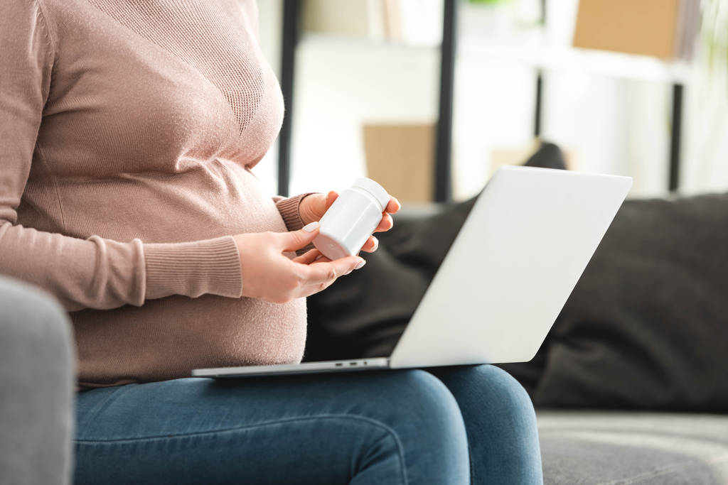 bijgesneden weergave van zwangere vrouw met pillen en het hebben van online overleg met de arts op laptop  - Foto, afbeelding