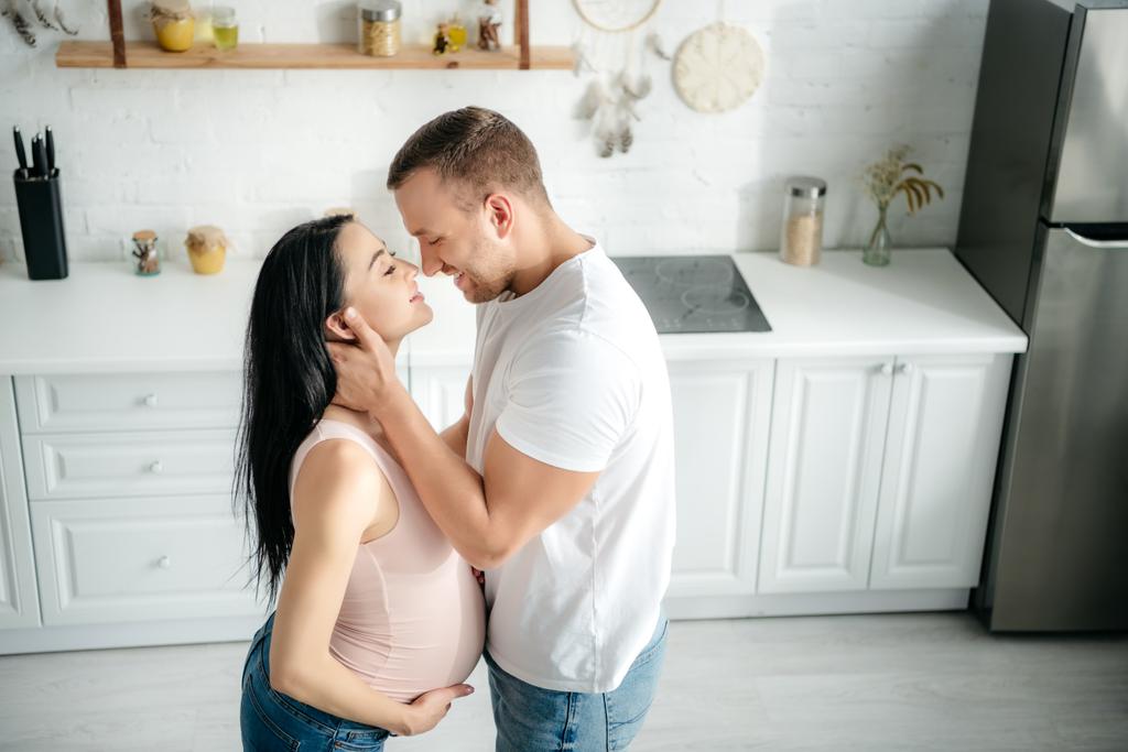 smiling husband hugging beautiful pregnant wife in kitchen - Photo, Image