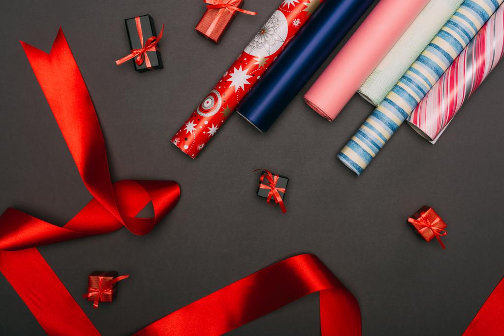 top view of wrapping paper rolls, ribbon and little gift boxes on black - 写真・画像