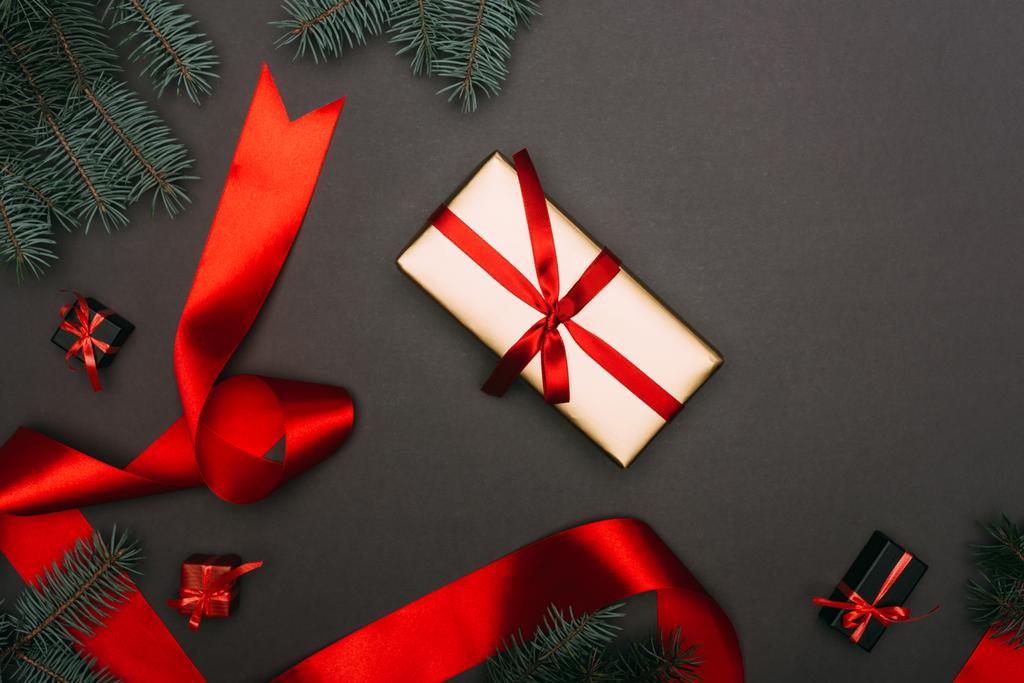 πάνω όψη κόκκινης κορδέλας και χριστουγεννιάτικων κουτιών δώρου με κλαδιά ερυθρελάτης σε μαύρο χρώμα - Φωτογραφία, εικόνα