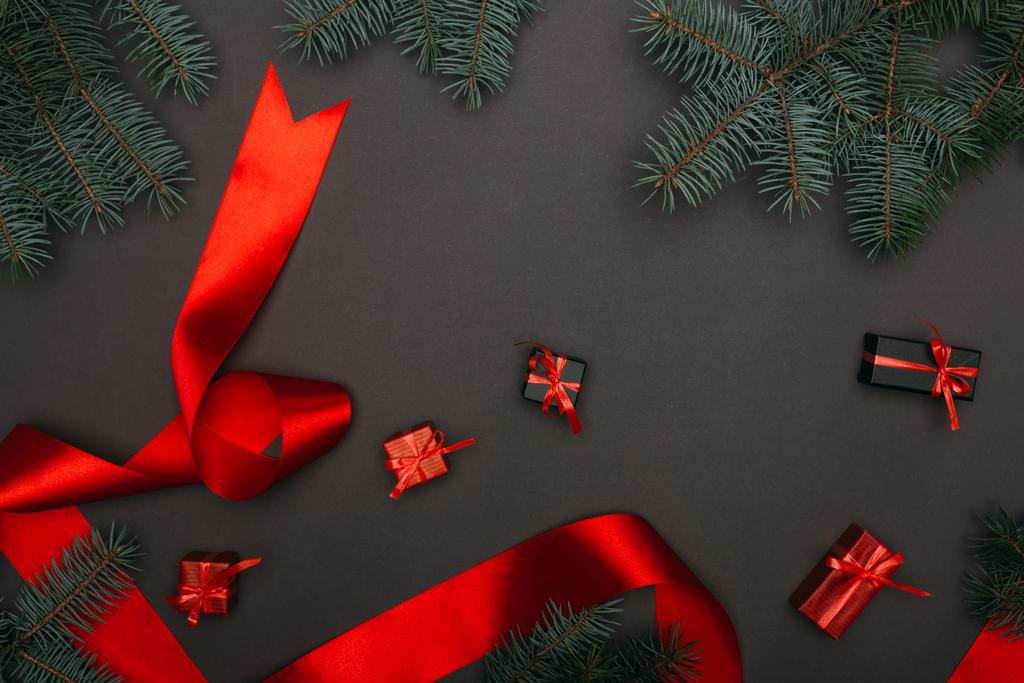 верхний вид рождественских подарочных коробок и красной ленты с еловыми ветвями на черном
 - Фото, изображение