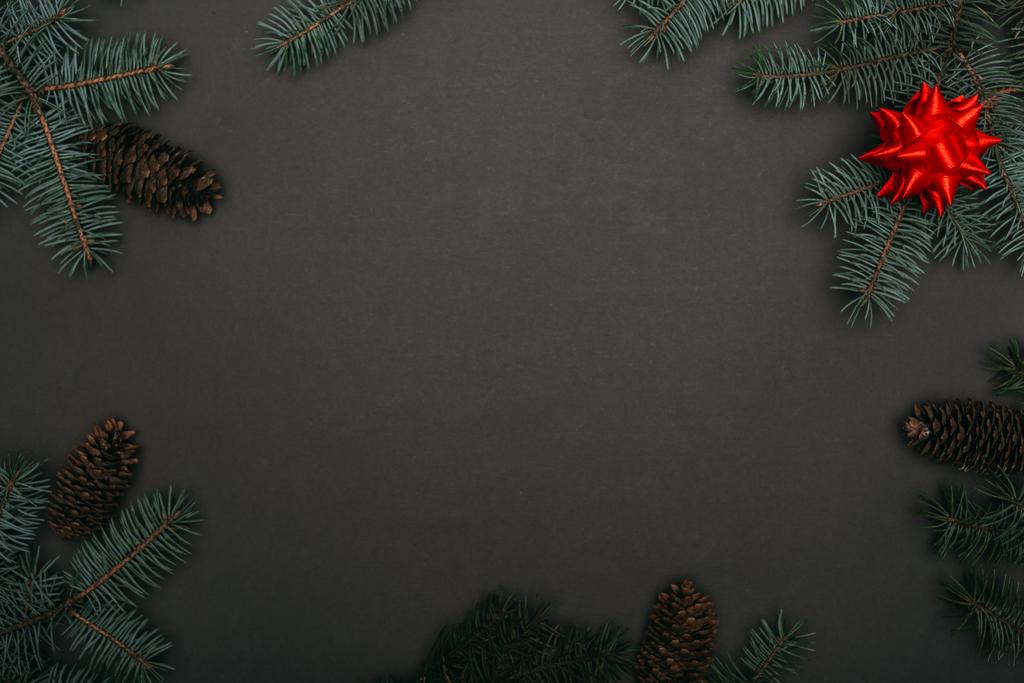 Spruce dalları, çam kozalakları ve siyah üzerine kırmızı fiyonk olan noel çerçevesinin üst görüntüsü - Fotoğraf, Görsel