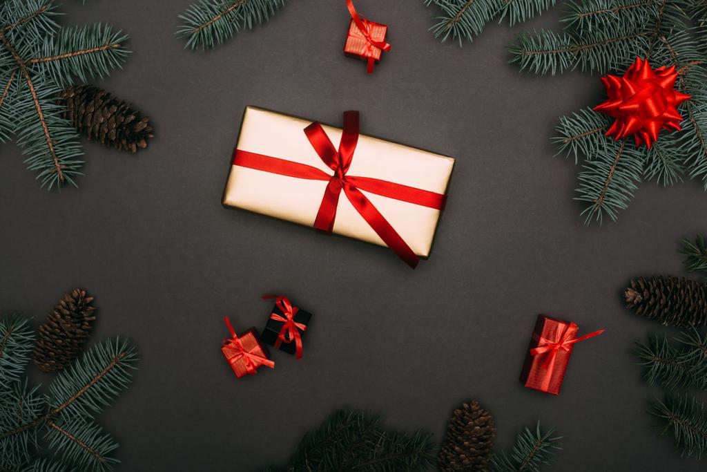 vrchní pohled na vánoční dárkové krabice se smrkovými větvemi a borovými šiškami na černé - Fotografie, Obrázek