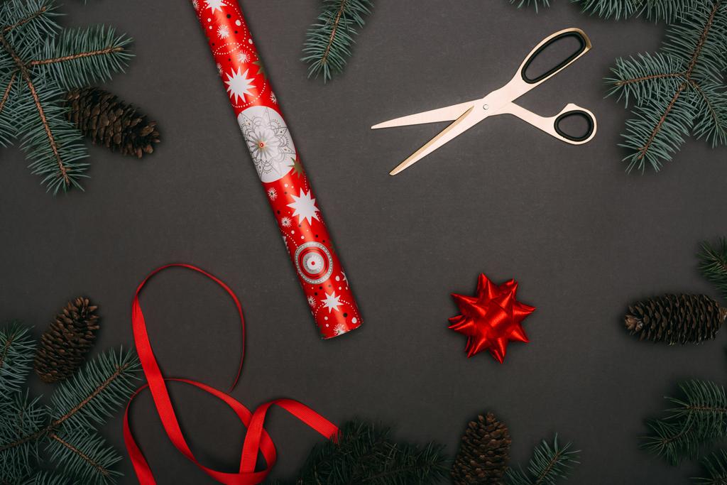 vue de dessus du rouleau de papier d'emballage de Noël, des ciseaux, du ruban et de l'arc dans le cadre des branches d'épinette et des cônes de pin sur noir
 - Photo, image