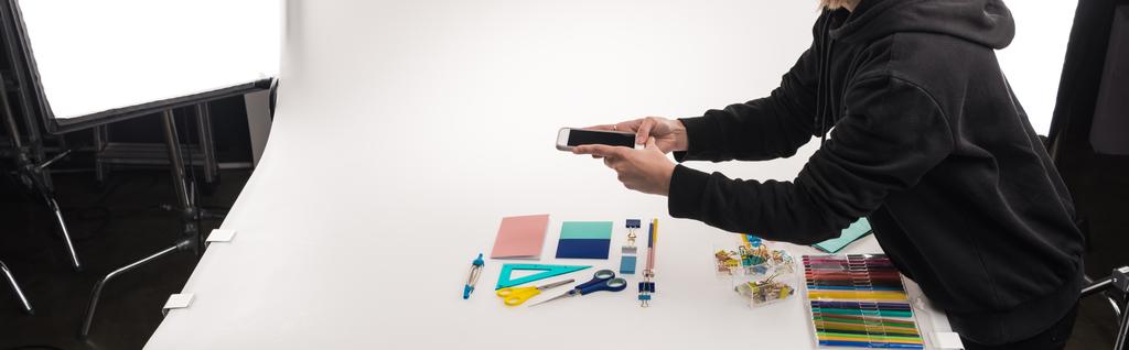 cropped view of commercial photographer making photos of office supplies on smartphone, panoramic shot - Photo, Image