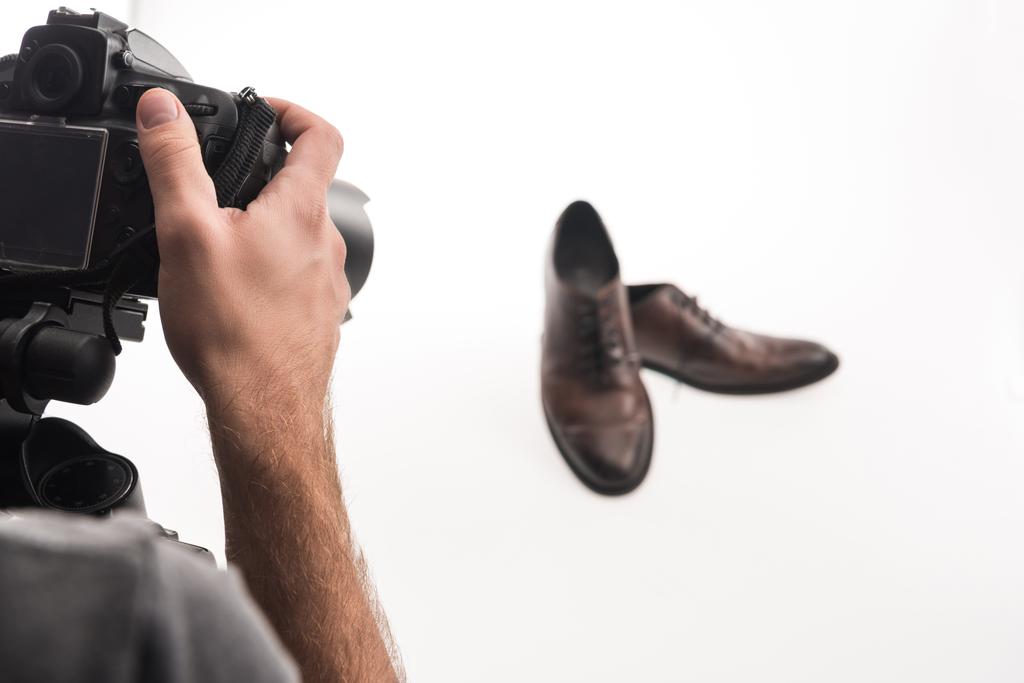 обрезанный вид мужчины фотографа, делающего коммерческую фотосессию мужской обуви на белом
 - Фото, изображение