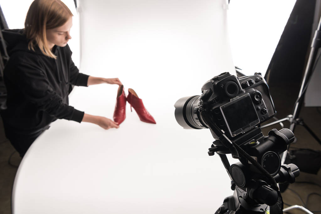 φωτογράφος κάνοντας εμπορική φωτογράφιση των γυναικείων κόκκινων παπουτσιών φτέρνα σε λευκό - Φωτογραφία, εικόνα