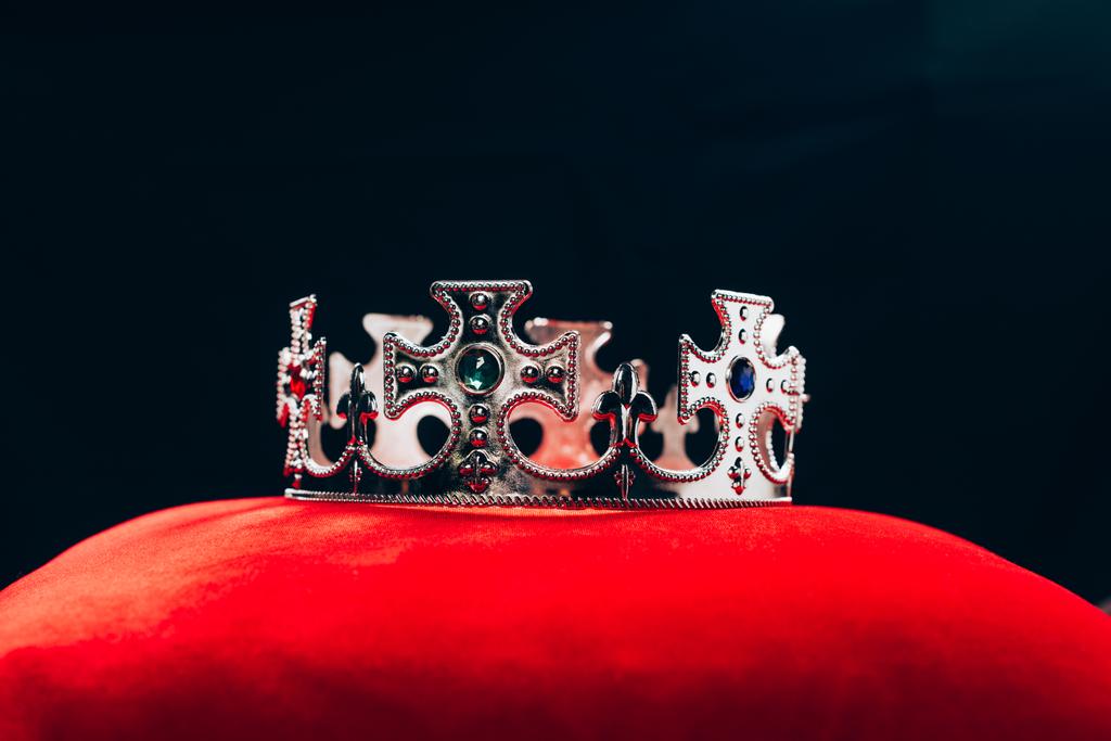 oude zilveren kroon met edelstenen op rood kussen, geïsoleerd op zwart - Foto, afbeelding