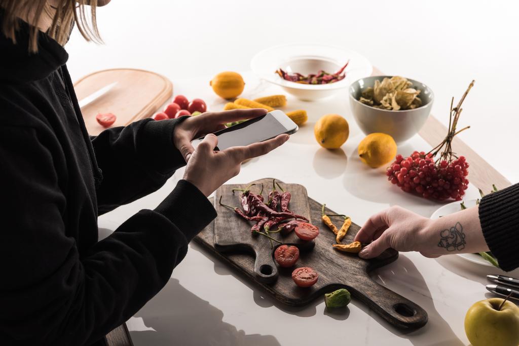 vista recortada de dos fotógrafos haciendo composición de alimentos para la fotografía comercial en el teléfono inteligente en la mesa de madera
 - Foto, Imagen