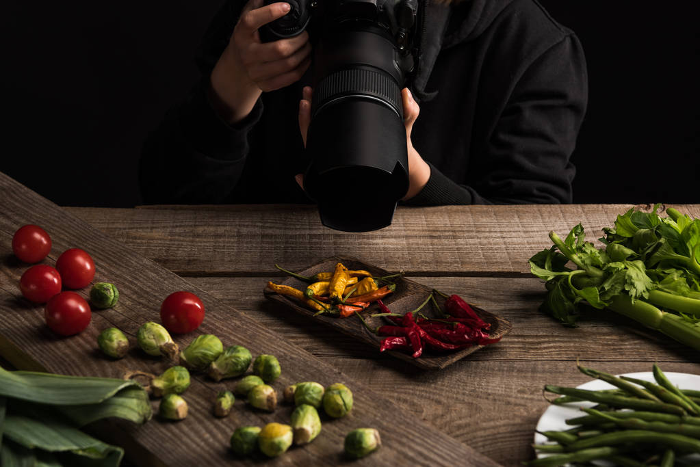 vista recortada de fotógrafa haciendo composición de alimentos para fotografía comercial y tomando fotos en cámara digital en mesa de madera
 - Foto, imagen