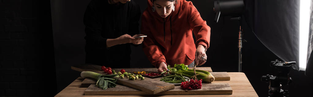 vista recortada de dos fotógrafos haciendo la composición de alimentos para la fotografía comercial en el teléfono inteligente, plano panorámico
 - Foto, Imagen