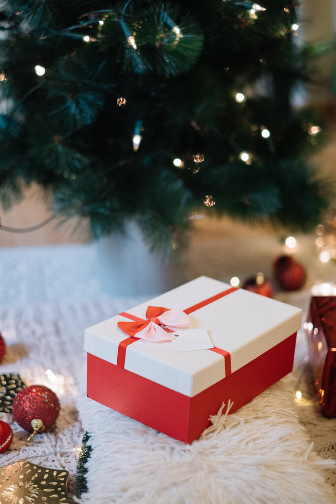 Caja de regalo decorada blanca y roja bajo el árbol de Navidad
 - Foto, imagen