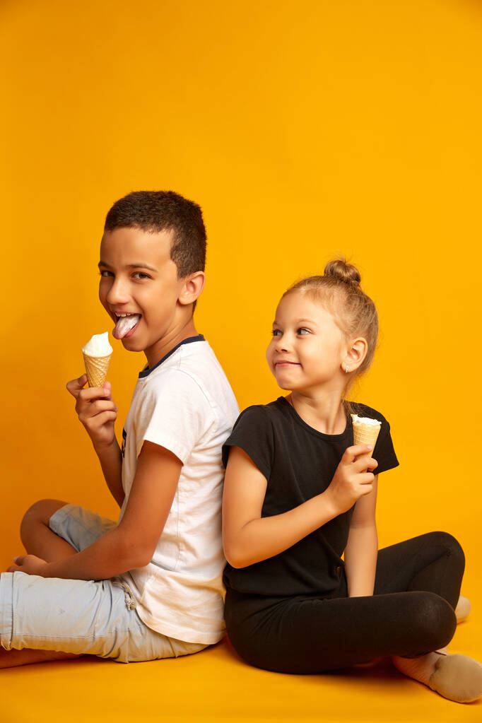 vicces gyerekek enni vanília fagylalt egy gofrisütő kúp sárga alapon, vidám testvér és testvér - Fotó, kép