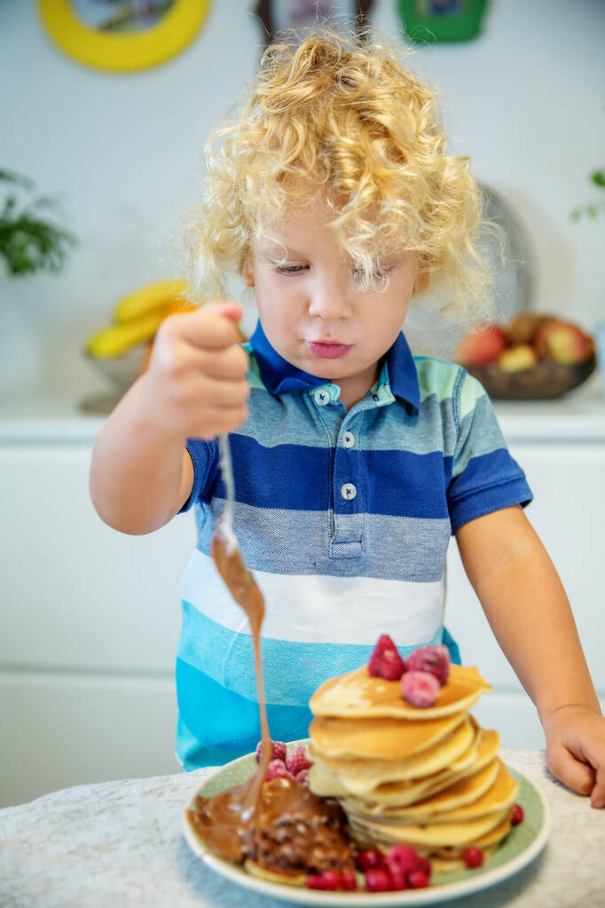 Маленький кучерявий хлопчик їсть солодкі млинці
 - Фото, зображення