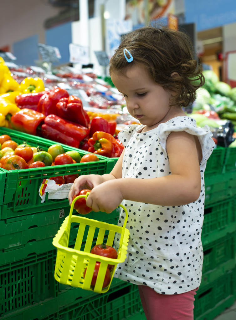 Pikkutyttö ostaa tomaatteja supermarketista. Lapsi pitää pieni bas
 - Valokuva, kuva